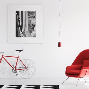 Può includere: Una bicicletta rossa con ruote bianche, una poltrona rossa imbottita a forma di uovo con sottili gambe in metallo, una piccola lampada a sospensione rossa e una grande fotografia quadrata in bianco e nero di un treno su una parete.