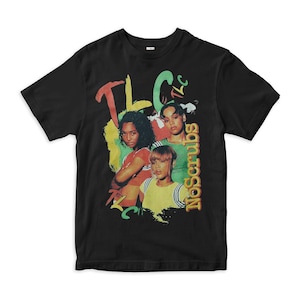 Op de afbeelding: Een zwart t-shirt met korte mouwen en een grafische print van de muziekgroep TLC. Het ontwerp bevat de tekst TLC en No Scrubs in kleurrijke, gestileerde letters, geplaatst over een foto van de drie leden van de muziekgroep.