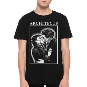 May include: A black t-shirt featuring a white graphic print of two people wearing face masks and embracing. The word ARCHITECTS is printed in white capital letters above the rectangular frame containing the stippled black and white illustration.