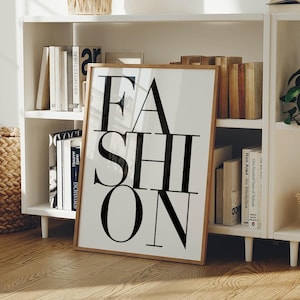 Könnte beinhalten: Ein rechteckiger gerahmter Wandkunstdruck mit dem Wort FASHION in großen, fetten, schwarzen serifenlosen Großbuchstaben, die vertikal auf einem weißen Hintergrund angeordnet sind. Der Druck befindet sich in einem hellen Holzrahmen mit schlichtem Design.