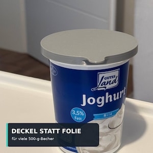 Peut inclure: Un pot de yaourt bleu et blanc avec un couvercle en plastique gris. L'étiquette porte le texte Gutes Land Joghurt, 3,5% Fett et Mild. Une boîte de superposition sombre en bas affiche le texte DECKEL STATT FOLIE für viele 500-g-Becher.