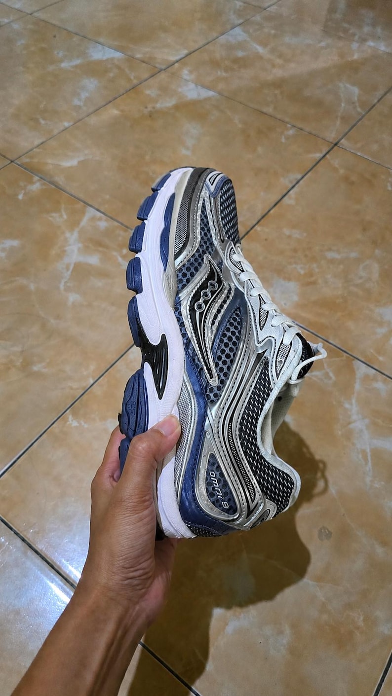 May include: A running shoe with a white, blue, and silver color scheme. The shoe features a mesh upper, a cushioned sole, and the text "omni 9" on the side. The shoe is designed for athletic activities.
