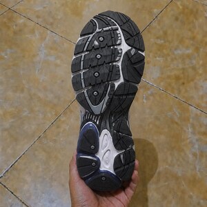 May include: A close-up view of the sole of a running shoe, held in a hand. The sole is black and white with a textured pattern for grip. The shoe has a blue accent near the heel.