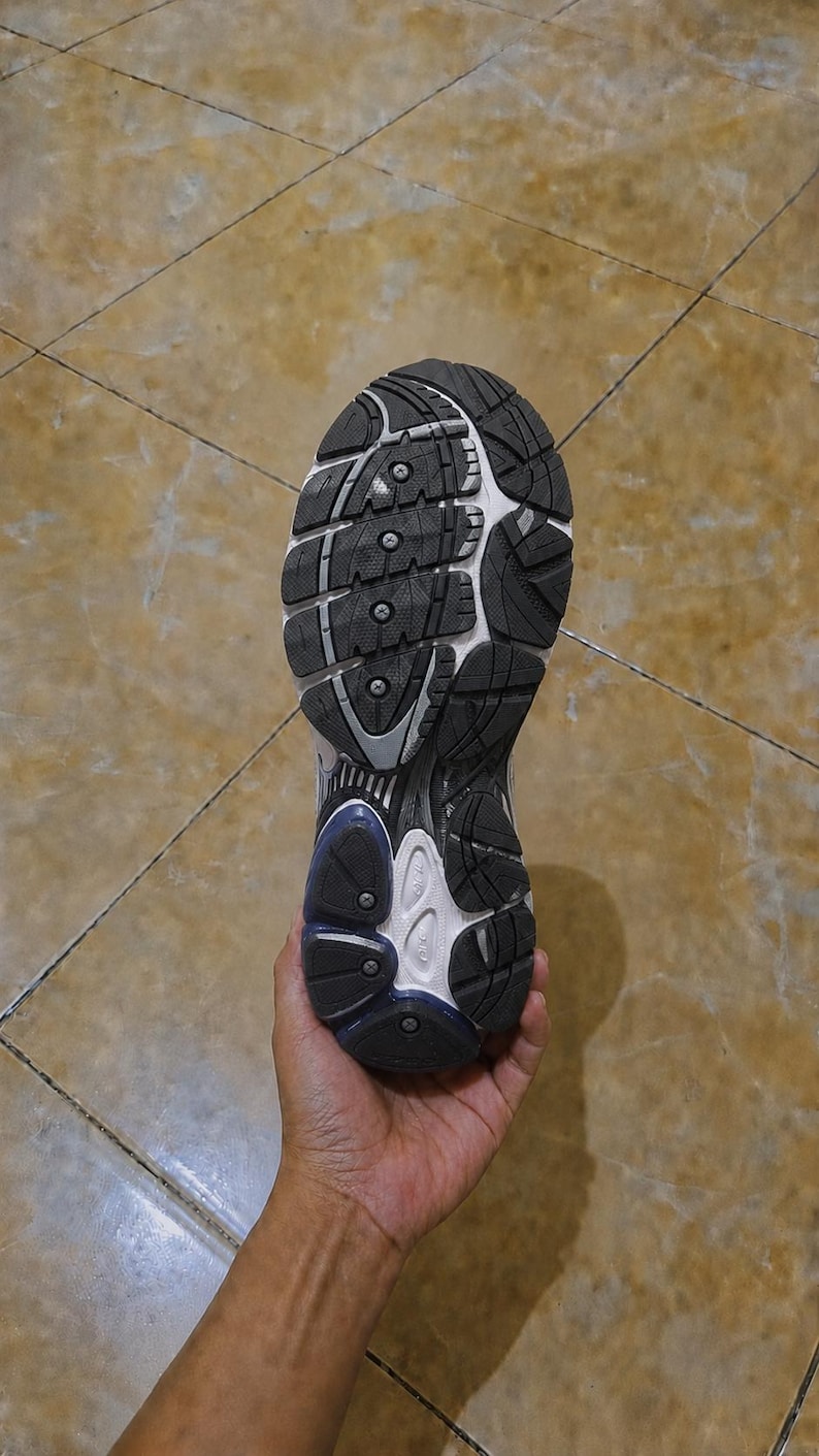 May include: A close-up view of the sole of a running shoe, held in a hand. The sole is black and white with a textured pattern for grip. The shoe has a blue accent near the heel.
