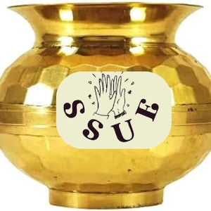 May include: A gold-colored, ornate pot with a wide mouth and a textured surface. A cream-colored oval sticker on the front displays the word "SUF" in dark brown letters, with a drawing of two hands clapping.