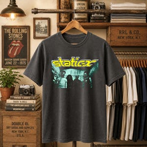 May include: A charcoal grey short-sleeve t-shirt featuring a graphic print on the chest. The graphic displays the yellow text "static-x" above a dark, stylised image of a band. The shirt has a crew neckline and a standard fit, presented on a hanger.