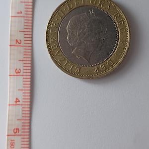 Peut inclure: Une pièce de deux livres sterling avec un centre argenté et un anneau extérieur doré. La pièce présente un profil d'une personne et du texte sur le bord. Un mètre ruban indique 150 cm.
