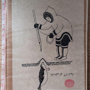 May include: An Inuit art print depicting a hunter spearing a seal. The black and white illustration shows a figure in a hooded parka and boots, with a spear aimed at a seal. The print includes text and a red circular stamp.