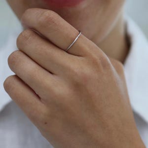 Könnte beinhalten: Ein dünner, polierter silberfarbener Metallring, der am Finger getragen wird. Der Ring zeichnet sich durch ein glattes, minimalistisches kreisförmiges Design mit einer reflektierenden Metalloberfläche aus, die das Licht einfängt.