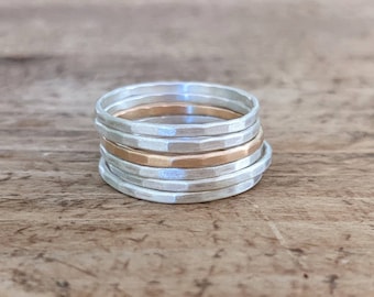 May include: Stack of six silver and gold hammered rings. The rings are stacked on a wooden surface.