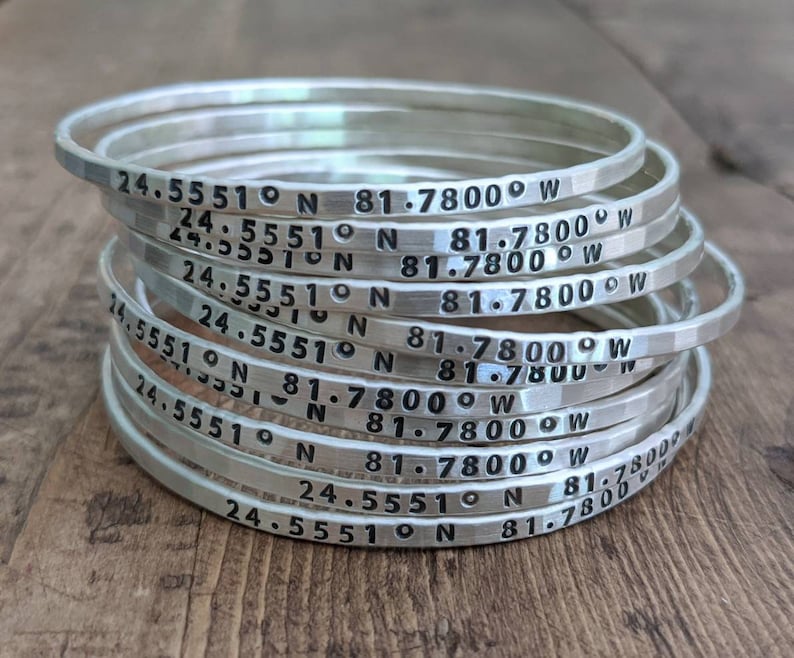 Peut inclure: Une pile de bracelets en argent grav&eacute;s avec les coordonn&eacute;es "24.5551&deg;N 81.7800&deg;W".