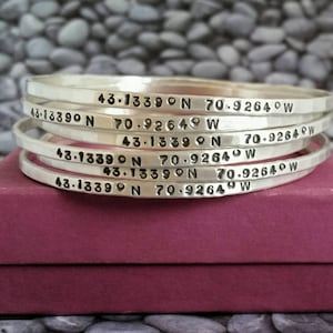 Peut inclure: Cinq bracelets en argent empil&eacute;s les uns sur les autres. Chaque bracelet est grav&eacute; avec les coordonn&eacute;es "43.1339&deg;N 70.9264&deg;W".
