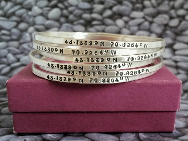 Peut inclure: Cinq bracelets en argent empil&eacute;s les uns sur les autres. Chaque bracelet est grav&eacute; avec les coordonn&eacute;es "43.1339&deg;N 70.9264&deg;W".