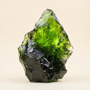 Angled view of a transparent green uncut gemstone specimen with olive smoky zones, reflective surfaces, and thick glass-like clarity for crystal collectors.
