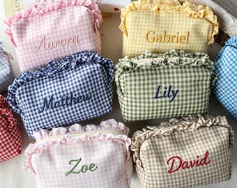 May include: A collection of rectangular fabric pouches featuring a gingham check pattern and ruffled top edges. Each pouch is embroidered with a unique name including Aurora, Gabriel, Matthew, Lily, Zoe, and David in various thread colors.