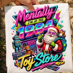 May include: A white t-shirt featuring a colorful 1980s-themed graphic with the text Mentally I'm at the 1984 Toy Store. The design includes Santa Claus wearing sunglasses, a retro robot, a boombox, a teddy bear, a yellow sports car, and a game controller.