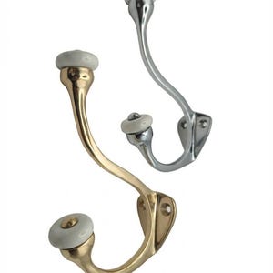 May include: Two wall-mounted coat hooks with a curved metal design. One hook features a polished gold-tone finish, while the other has a polished silver-tone finish. Both hooks are topped with a smooth, round white ceramic knob at each end.
