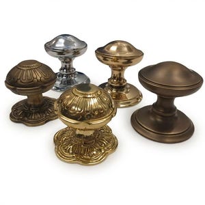 May include: A collection of five metal door knobs in various finishes including polished chrome, brass, and bronze. Some knobs feature a decorative fluted or petal-like design on the base and top, while others have a smooth, rounded surface.