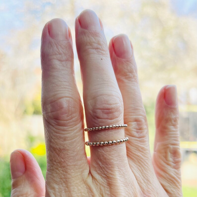 Puede incluir: Dos anillos de cuentas doradas apilados en un dedo. Los anillos est&aacute;n hechos de peque&ntilde;as cuentas redondas.