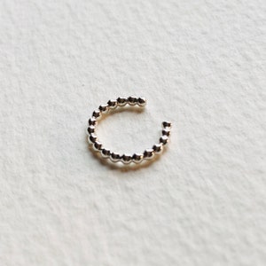 Puede incluir: Un ear cuff plateado con un diseño de cuentas. El brazalete se curva alrededor de la oreja, con pequeñas cuentas espaciadas uniformemente. El extremo abierto permite una fácil colocación.