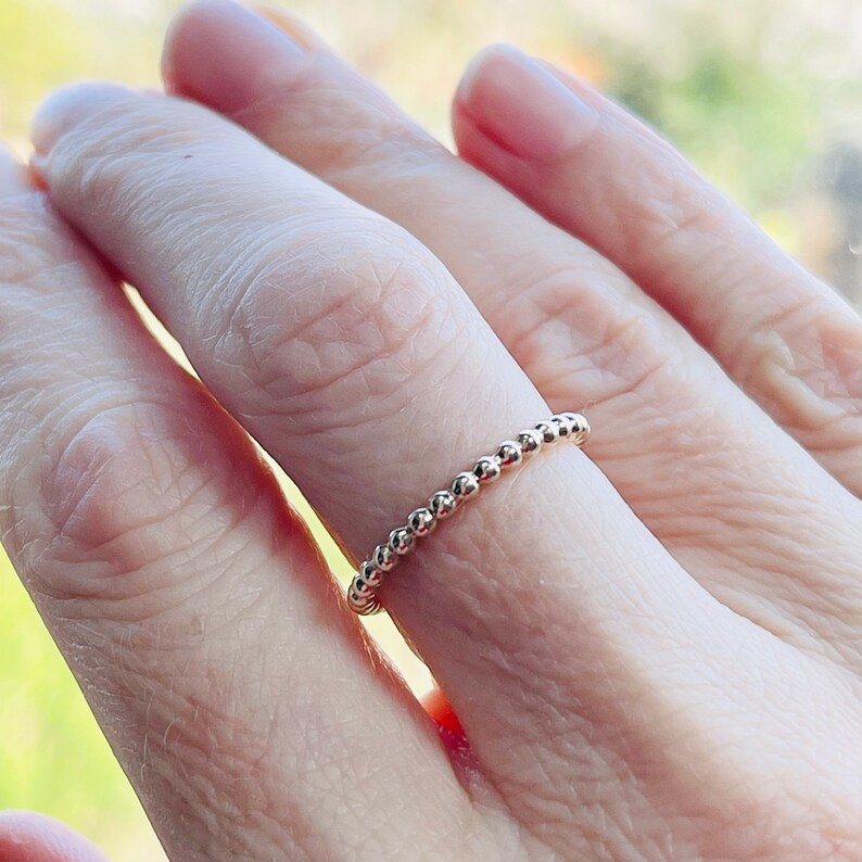 Puede incluir: Un delicado anillo de oro con cuentas, usado en un dedo.