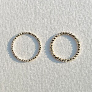 Puede incluir: Dos anillos de cuentas doradas sobre un fondo blanco. Los anillos est&aacute;n hechos de peque&ntilde;as cuentas redondas que est&aacute;n conectadas entre s&iacute; para formar un c&iacute;rculo.
