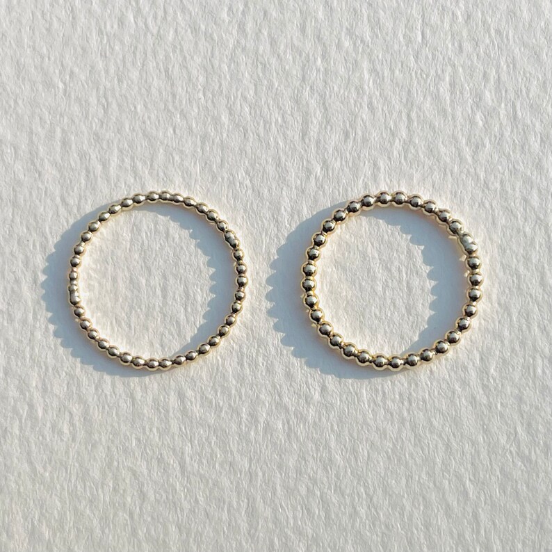 Puede incluir: Dos anillos de cuentas doradas sobre un fondo blanco. Los anillos est&aacute;n hechos de peque&ntilde;as cuentas redondas que est&aacute;n conectadas entre s&iacute; para formar un c&iacute;rculo.
