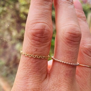 Puede incluir: Dos anillos de oro en un dedo. El anillo superior es de estilo cadena de eslabones delicados. El anillo inferior es una banda fina de peque&ntilde;as cuentas.