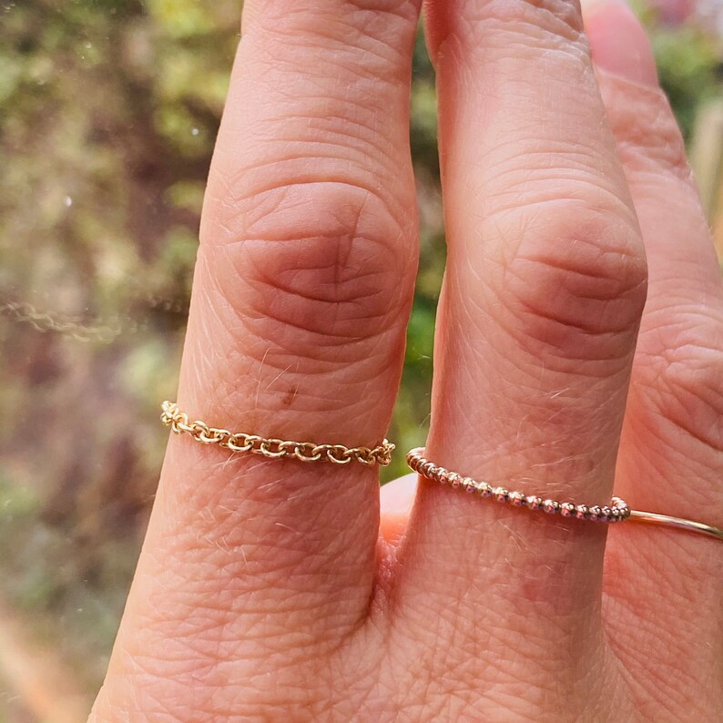 Puede incluir: Dos anillos de oro en un dedo. El anillo superior es de estilo cadena de eslabones delicados. El anillo inferior es una banda fina de peque&ntilde;as cuentas.