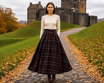 May include: A long, high-waisted, pleated skirt featuring a dark burgundy, forest green, and black plaid pattern. The skirt is paired with a long-sleeved, cream-colored knit sweater and brown leather ankle boots.