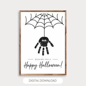 May include: A framed print featuring a black handprint spider with googly eyes hanging from a black spiderweb illustration. Below the spider, the text reads "WISHING YOU A Happy Halloween!" in black lettering on a white background.