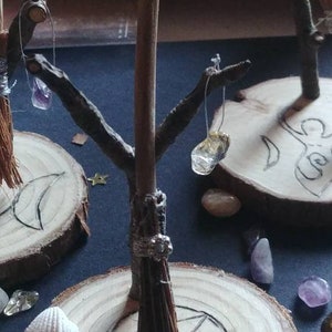 Pode incluir: Um conjunto de altar de madeira com um design de pentagrama, uma pequena vassoura e cristais pendurados em galhos.