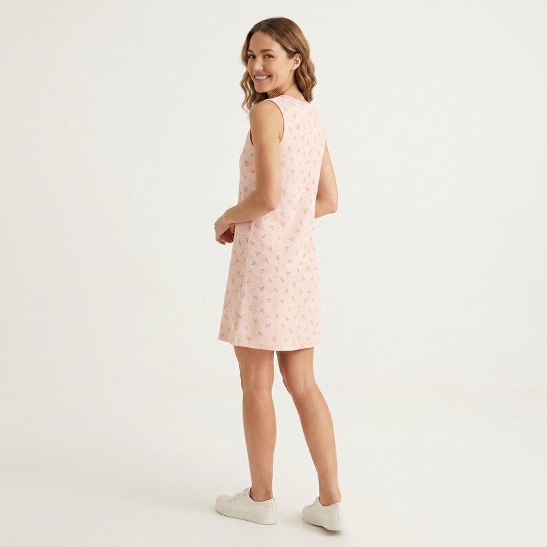 May include: A sleeveless, knee-length shift dress in a soft pale pink hue, featuring an all-over delicate floral pattern in a darker shade of pink. The garment has a simple round neckline and a straight, relaxed silhouette, paired with white sneakers.
