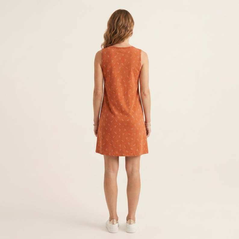 May include: A sleeveless knee-length dress in a burnt orange hue featuring a subtle, repeating white botanical pattern. The garment has a simple round neckline and a straight, relaxed silhouette that falls to the mid-thigh area.
