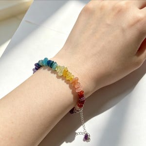May include: A bracelet composed of small, irregular, polished gemstone chips in a spectrum of rainbow colors including red, orange, yellow, green, blue, and purple. The bracelet features a silver-toned metal chain extender with a small dangling stone.