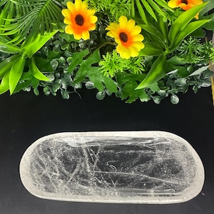May include: An oval-shaped clear crystal tray with a textured, cracked interior surface. The tray features a smooth, rounded outer rim and a translucent appearance, showcasing natural internal fractures throughout the clear stone material.