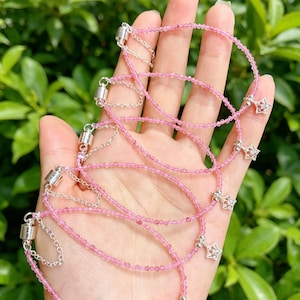 May include: A collection of delicate bracelets featuring small, faceted pink beads strung on thin wire. Each bracelet includes a silver-toned star-shaped charm with clear accents, a short silver chain segment, and a cylindrical magnetic clasp closure.