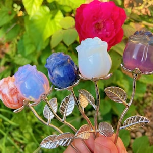 May include: Five decorative metal stems, each topped with a carved stone rose in orange, light blue, dark blue, white, and purple. Each silver-toned stem features detailed metal leaves and a secure base for the stone flower head.