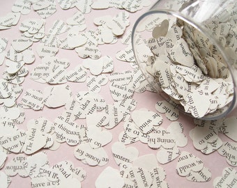 May include: A glass jar filled with white paper hearts, each with a different word printed on it. The hearts are scattered on a pink surface.