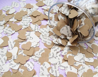 May include: Heart-shaped confetti made from book pages and kraft paper, scattered on a light purple surface. A clear glass is tipped over, spilling more heart confetti. The hearts have printed text.