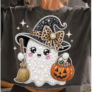 May include: A charcoal gray cropped sweatshirt featuring a graphic of a white ghost wearing a black witch hat with a leopard print bow. The ghost holds a brown broom and an orange jack-o'-lantern bucket, decorated with sparkling rhinestones.