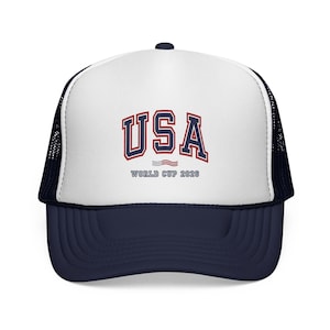 May include: A trucker hat with a white front panel and a navy blue brim and mesh back. The front features the word "USA" in red and navy blue lettering, with "WORLD CUP 2026" below.