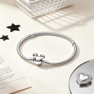 Puede incluir: Una pulsera plateada con un cierre en forma de Mickey Mouse y un charm en forma de coraz&oacute;n con borde de cristal. La pulsera est&aacute; sobre una superficie blanca con una cesta de alambre blanca y decoraciones en forma de estrella negra.