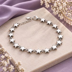 May include: A silver-toned chain bracelet featuring a series of evenly spaced, polished star-shaped charms connected by small circular links. The bracelet includes a lobster claw clasp and an adjustable extender chain with a small oval tag at the end.