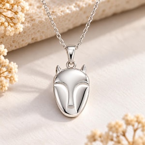 May include: A polished silver-tone pendant shaped like a stylized fox head, suspended from a delicate matching silver-tone chain. The pendant features smooth, reflective surfaces with defined contours representing ears and a snout, creating a sleek look.