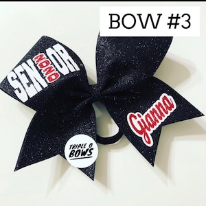 Puede incluir: Un lazo de animadora negro brillante con las palabras "SENIOR" y "Gianna" en rojo y blanco. El lazo tambi&eacute;n presenta una peque&ntilde;a pegatina redonda con el texto "TRIPLE O BOWS". Es un accesorio para el cabello.