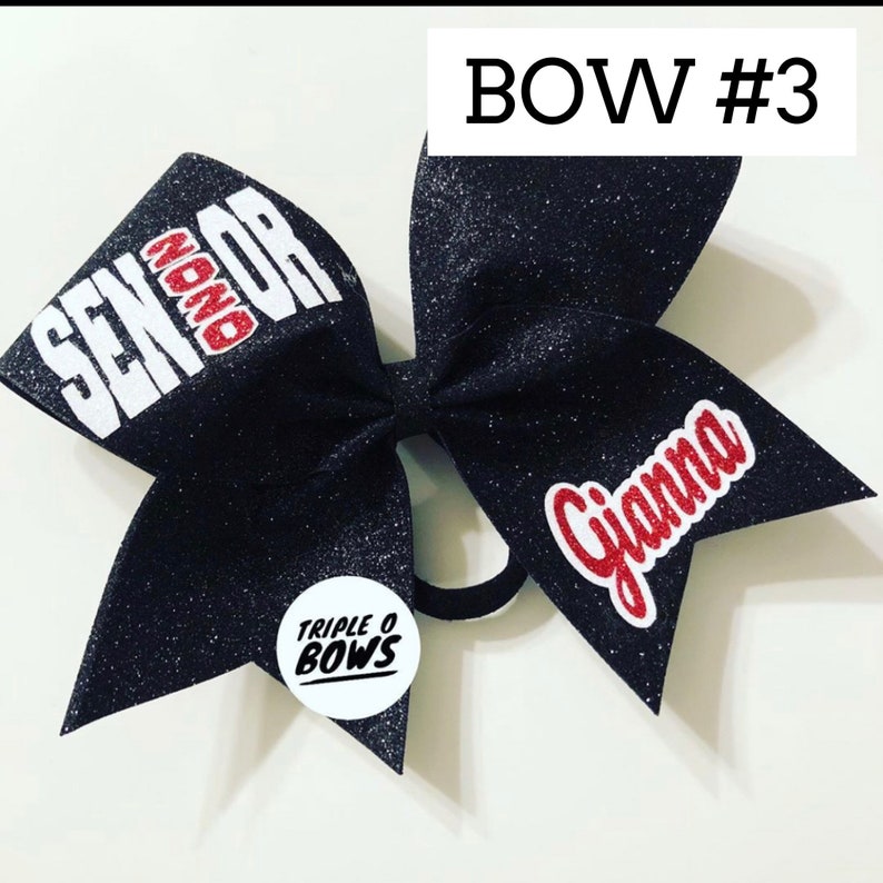 Puede incluir: Un lazo de animadora negro brillante con las palabras "SENIOR" y "Gianna" en rojo y blanco. El lazo tambi&eacute;n presenta una peque&ntilde;a pegatina redonda con el texto "TRIPLE O BOWS". Es un accesorio para el cabello.