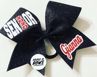 May include: Black glitter cheer bow with white text that says "Senior" and red text that says "#NoMore". The bow also has red text that says "Gianna" and a white circle with black text that says "Triple O Bows".