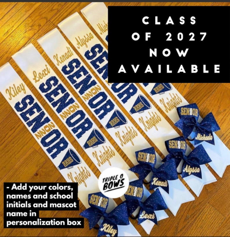 Puede incluir: Bandas de graduaci&oacute;n blancas y azul marino con letras doradas y lazos de purpurina azul marino. Las bandas tienen la palabra "SENIOR" y los nombres de los graduados. Tambi&eacute;n se ve el texto "CLASS OF 2027 NOW AVAILABLE".
