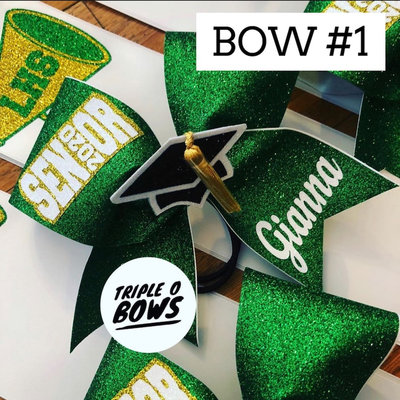 Puede incluir: Lazo de animadora con purpurina verde con el texto "Gianna" en blanco. El lazo presenta un gorro de graduaci&oacute;n y el texto "SENIOR 2020". El lazo est&aacute; etiquetado como "BOW #1" y tiene el logotipo "TRIPLE O BOWS".